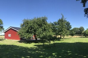 A red barn with a small porch, surrounded by a grassy field and trees. - Holiday wooden house (Neustadt)