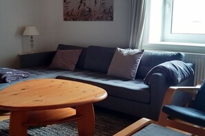 Een woonkamer met een grijze bank, een houten salontafel en een blauwe fauteuil.