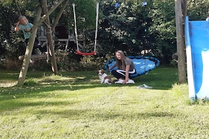 Ein grünes Freigelände mit Schaukel, kleinem aufblasbaren Pool und Rutsche.