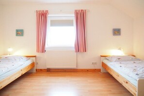 Een kamer met twee eenpersoonsbedden, een raam met gordijnen, een radiator en twee wandlampen.