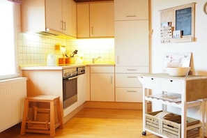 Eine Küche mit weißen Schränken, einem Holzschemel, einem kleinen Wagen und einer Kreidetafel an der Wand.