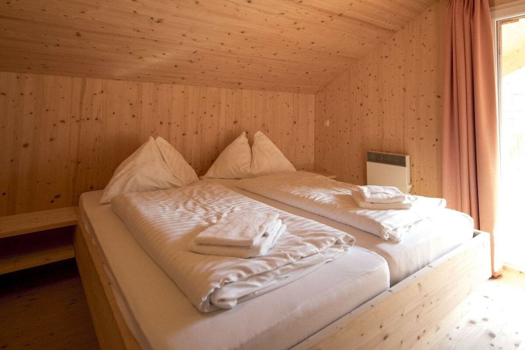A wooden cabin room with two beds, each with pillows and folded towels.