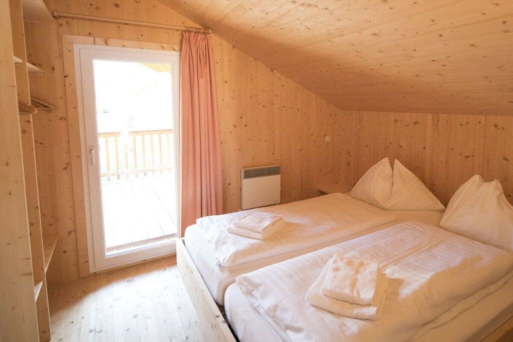A room with a wooden ceiling and walls, a bed with white bedding, a window with a curtain, and an air conditioning unit.