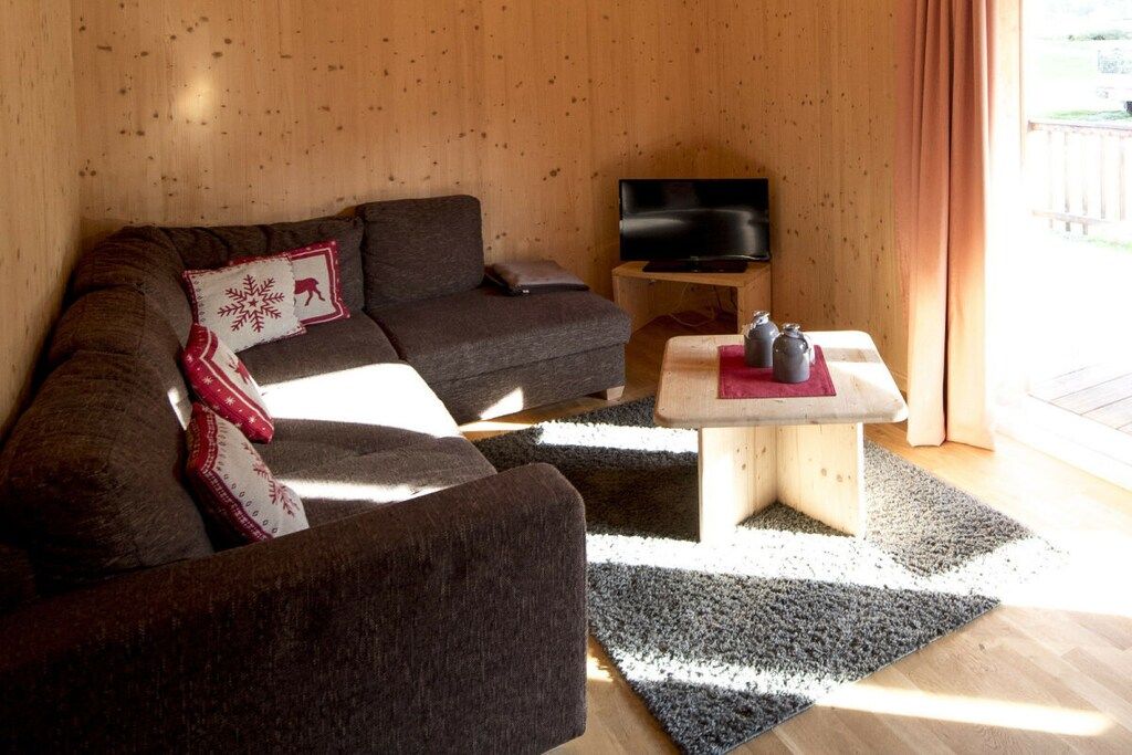 A cozy living room with a sofa, a coffee table, a television, and a window with curtains.