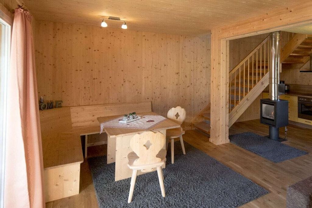 A wooden interior with a dining area, a staircase, and a wood-burning stove.