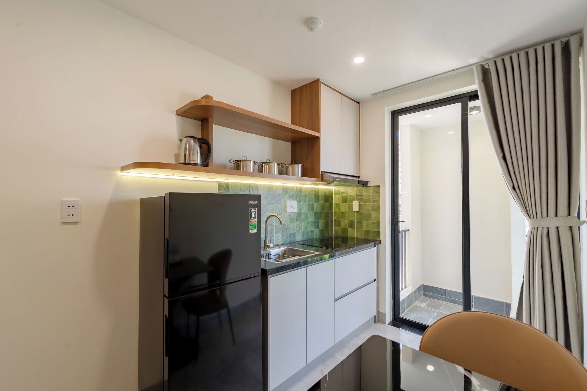 Una cocina compacta con refrigerador, un lavamanos y un estante de madera encima.