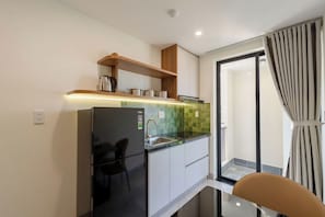 A compact kitchen with a refrigerator, a sink, and a wooden shelf above it. - Weal Hotel & Apartment (Da Nang)