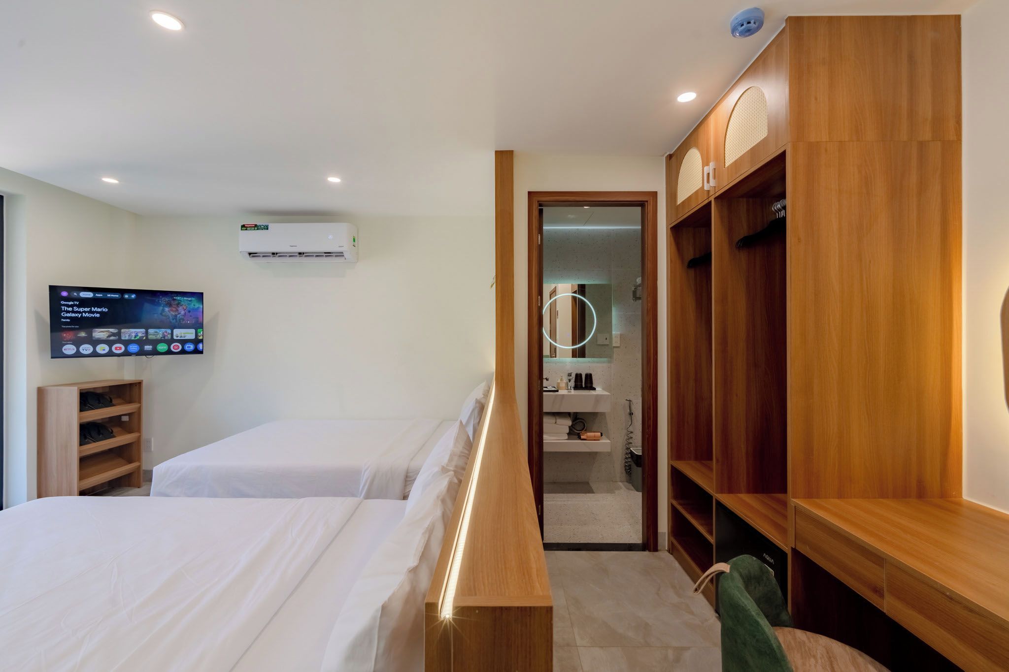 Habitación de hotel con dos camas, un televisor montado en la pared, un armario y un espejo.