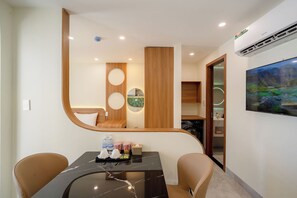 A hotel room with a dining area, a kitchen, and a large window with a painting. - Weal Hotel & Apartment (Da Nang)