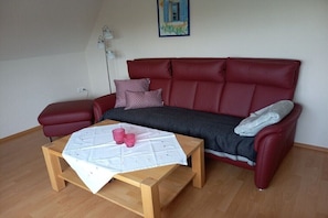 A red leather sofa with a grey throw blanket and a small wooden table with a white tablecloth and pink cups.