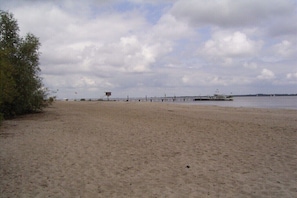 A sandy beach with a pier extending into the water, a small building, and a cloudy sky.