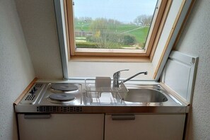 Une cuisine compacte équipée d’une cuisinière intégrée, d’un évier et d’une fenêtre donnant sur un paysage verdoyant.