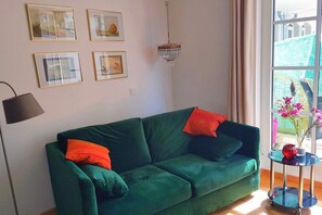 Un canapé vert avec des coussins orange, un lampadaire noir et un lustre.