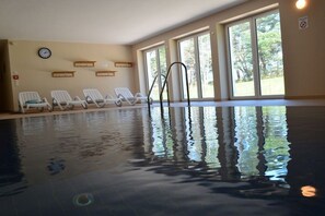 Ein Innenpool mit klarem Wasser, eine Uhr an der Wand und eine Reihe weißer Liegestühle.