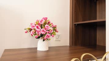 Una mesa de comedor con un jarrón blanco lleno de flores rosadas, una estantería de madera y sillas doradas con detalles en forma de lazo.