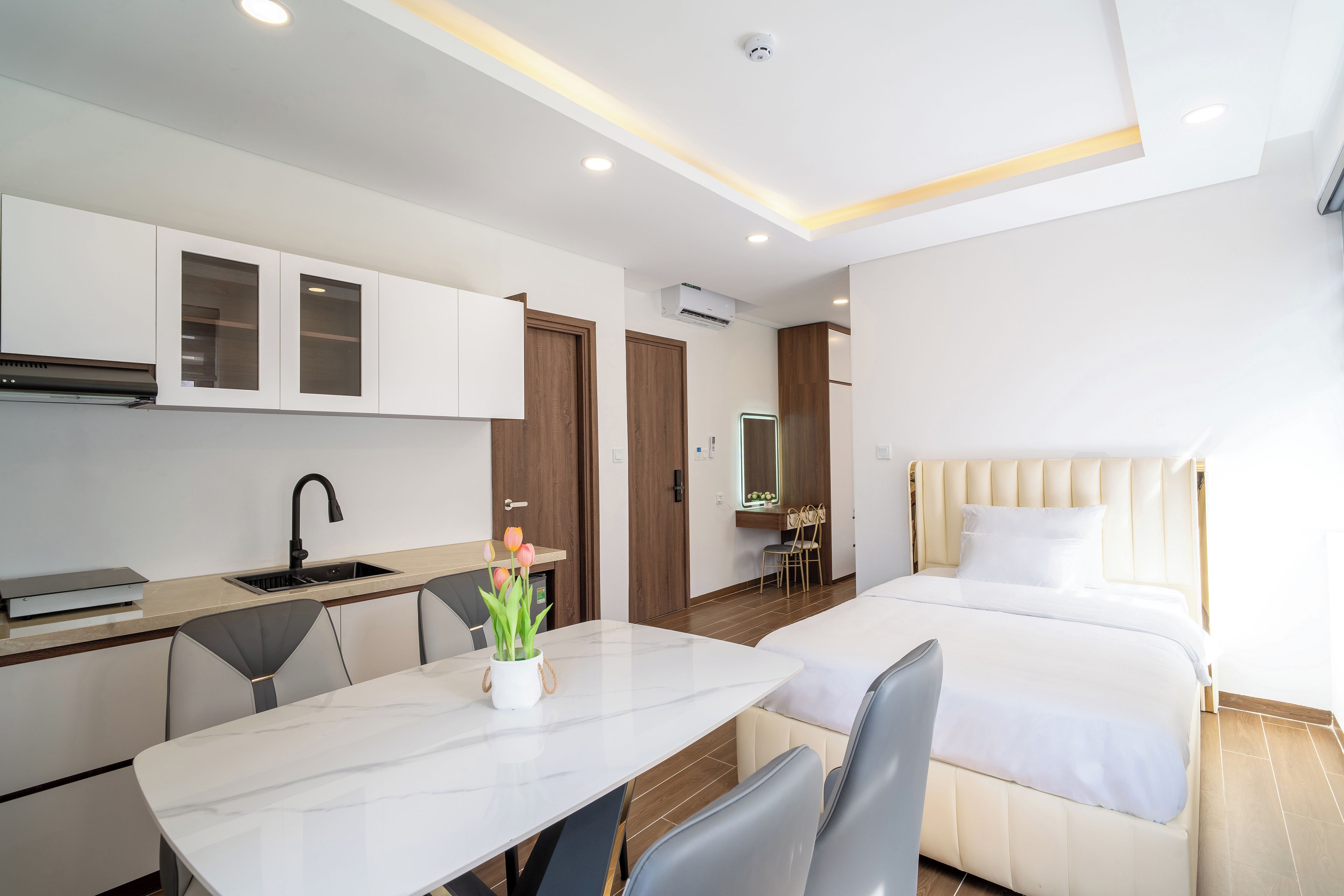 A modern hotel room with a bed, a desk, a chair, a small kitchenette, and a bathroom.