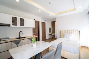 Habitació d'hotel moderna amb llit, escriptori, cadira, petita cuina i bany.