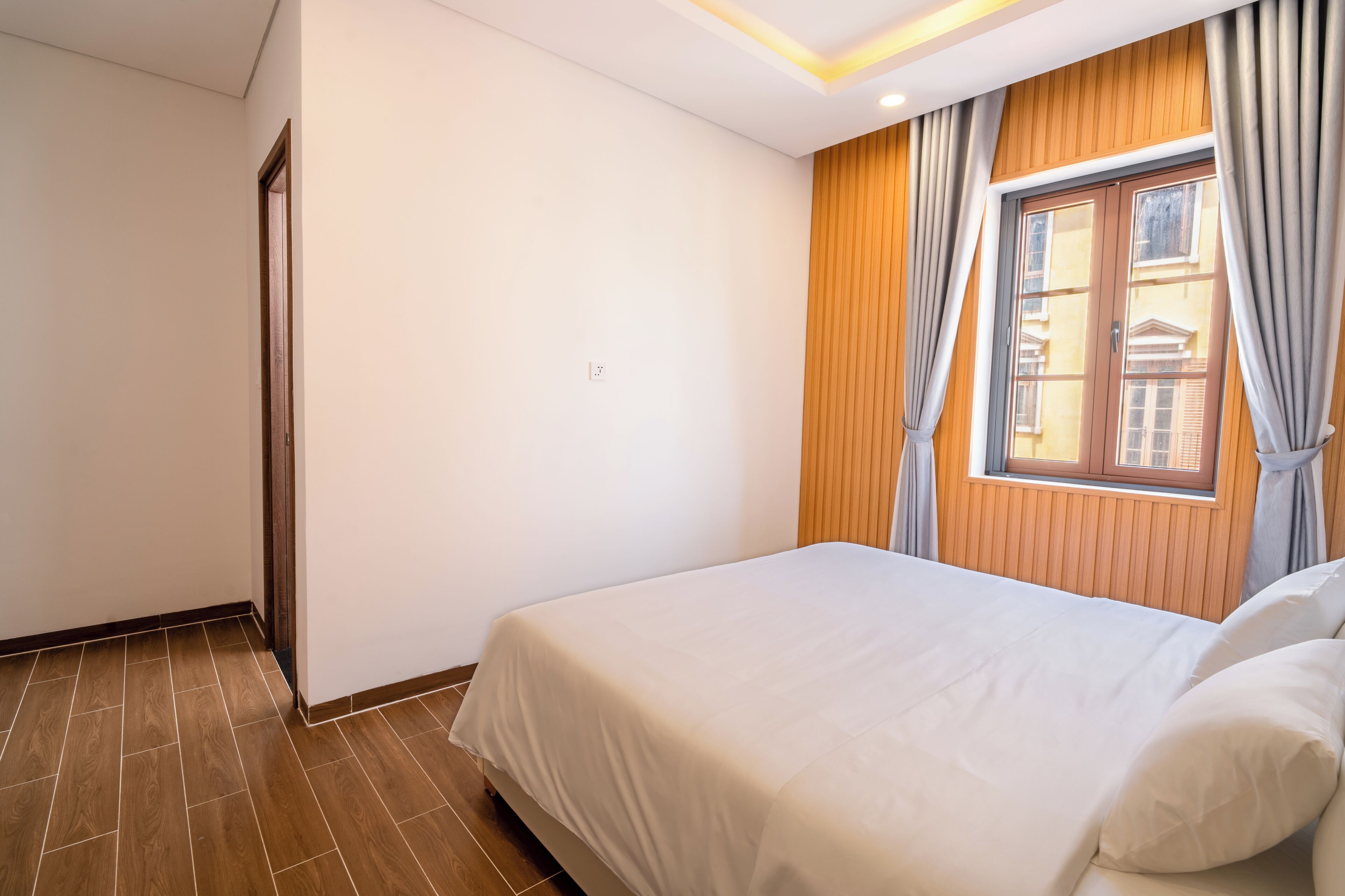 Een hotelkamer met een bed, houten lambrisering, een raam met gordijnen en een deur.