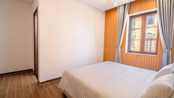 Een hotelkamer met een bed, houten lambrisering, een raam met gordijnen en een deur.