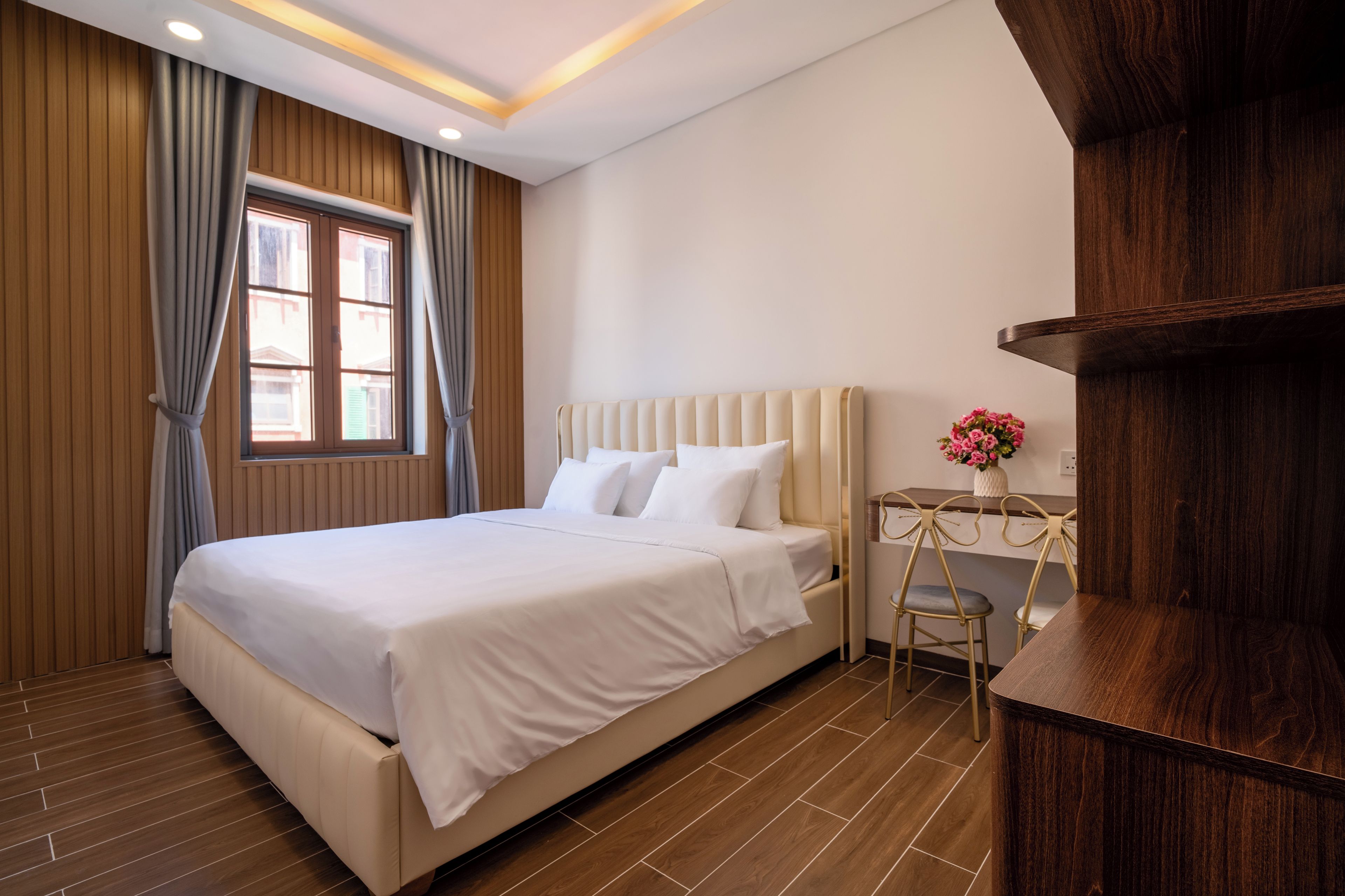 A modern bedroom with a large bed, wooden panel walls, a window with curtains, a bedside table with a vase, and a wooden cabinet.