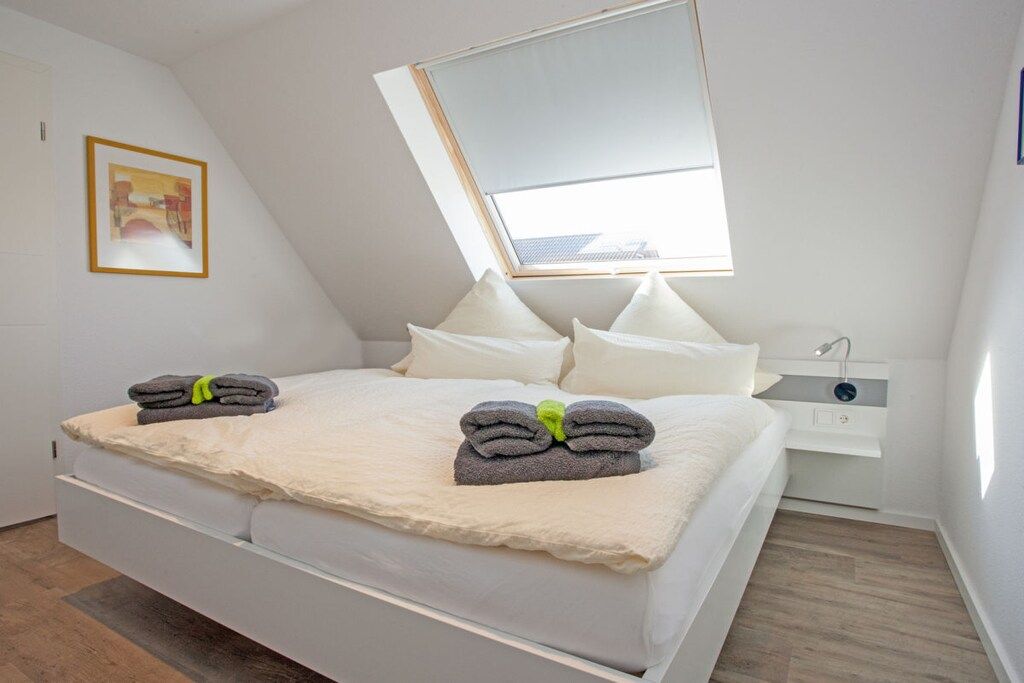 A modern bedroom with a skylight, a bed with white bedding, and a bedside table with a lamp.