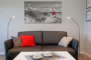 Un salon moderne avec un canapé en cuir noir, deux lampadaires et une photographie en noir et blanc encadrée accrochée au mur.
