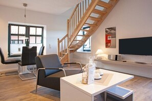 Ein modernes Wohnzimmer mit einer Holztreppe, einem Flachbildfernseher und einer Sitzecke mit Sesseln.