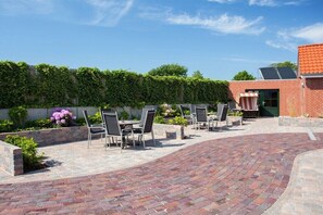 Une terrasse extérieure avec un sol en briques, un mur en briques agrémenté de plantes et des sièges d’extérieur.