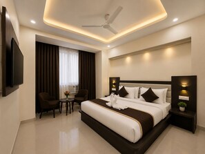 Habitación de hotel moderna con una cama grande, televisión de pantalla plana, ventilador de techo y una pequeña mesa con sillas.