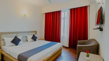 Habitación de hotel con una cama, una silla, una mesita y una ventana con cortinas rojas.