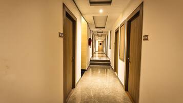 Un pasillo de hotel con puertas a ambos lados, suelo de mármol e iluminación empotrada en el techo.