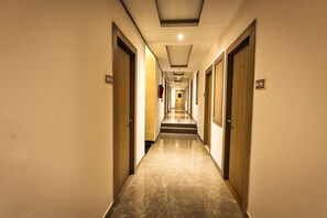 Un pasillo de hotel con puertas a ambos lados, suelo de mármol e iluminación empotrada en el techo.