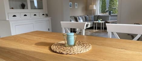 Un comedor con una mesa de madera, sillas blancas y un mantel tejido.