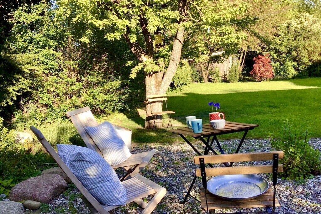 An outdoor seating area with a wooden bench and a chair, a metal tray, and a table with a mug and a cup.