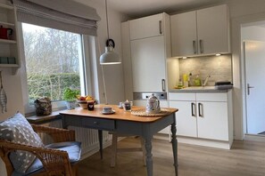 A kitchen with white cabinets, a wooden table, and a wicker chair. - Holiday home in Klein Waabs with Wi-Fi (Klein Waabs)