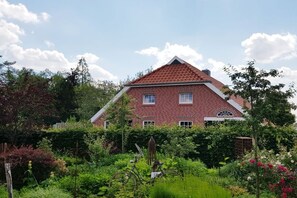 A two-story brick house with a red-tiled roof, surrounded by lush greenery and a variety of plants. - Country House Moor and Sea *2* (Ostgroßefehn)