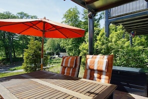 An outdoor seating area with a table and chairs, a red umbrella, and a view of trees and a building in the background. - Holiday apartment with 1 bedroom (Sellin)