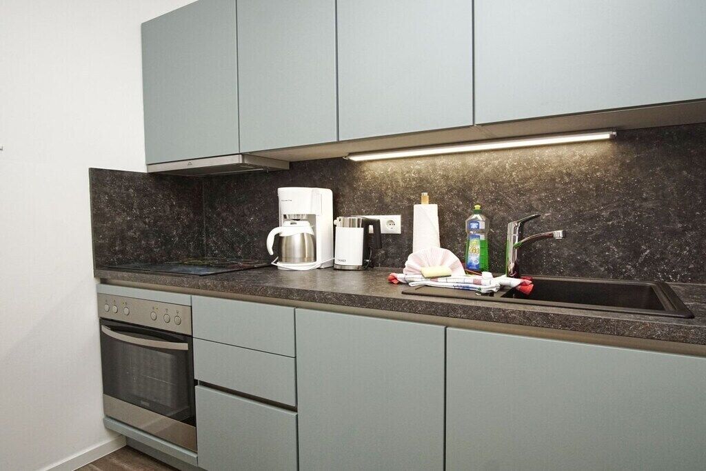 A modern kitchen with grey cabinets, a built-in oven, a coffee maker, and a sink.