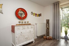 Een kamer met een witte ladekast, een rode spiegel, een radiator, een houten paal en een raam met gordijnen.