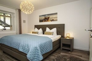 Een slaapkamer met een groot bed, een nachtkastje, een aan de muur hangend schilderij en een plafondlamp.
