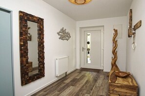 A hallway with a wooden-framed mirror, a radiator, a wooden sculpture, and a door with a frosted glass panel. - Holiday apartment with 1 bedroom (Sellin)