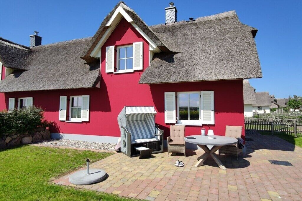 A red house with a thatched roof, a patio with outdoor furniture, and a small garden.