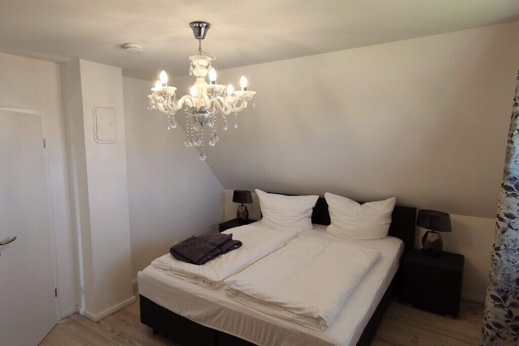 A bedroom with a large bed, two bedside tables, a chandelier, and a door.
