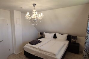 A bedroom with a large bed, two bedside tables, a chandelier, and a door. - Thatched house "Aquata" (Zierow)