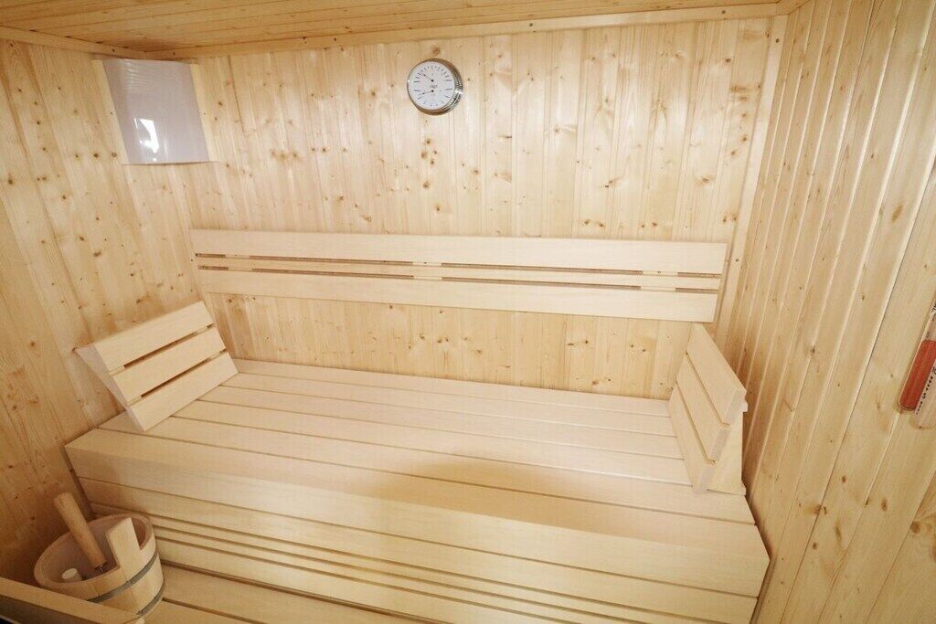 A wooden sauna with benches, a wall-mounted heater, and a small wooden bucket.