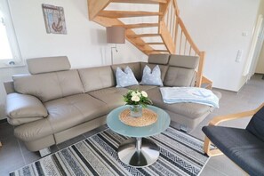 A modern living room with a sectional sofa, a glass coffee table, and a patterned rug. - Thatched house "Koje15" (Zierow)