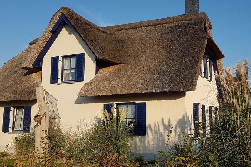 A traditional house with a steep thatched roof and white walls.