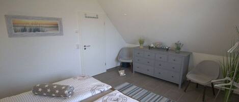 A bedroom with two beds, a dresser, a chair, and a painting on the wall.
