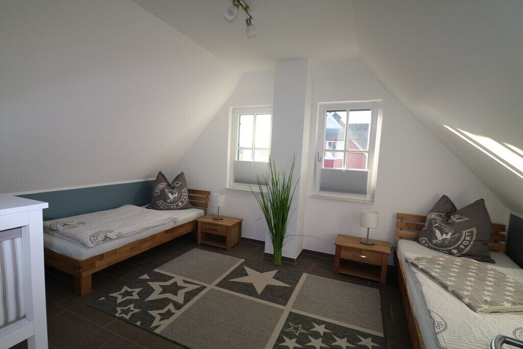 A small, well-lit room with two beds, a window, and a plant.