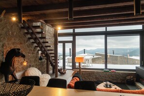 Een gezellig interieur met een stenen muur, een houten trap en een groot raam met uitzicht op besneeuwde bergen.